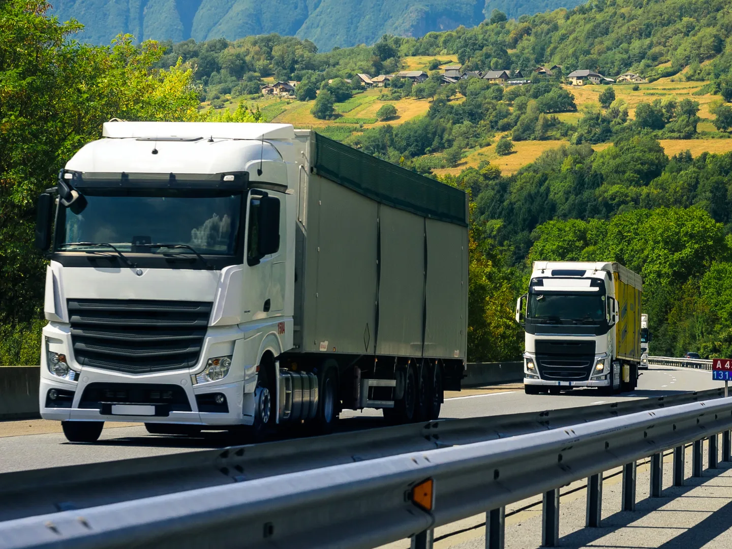 Articulated tankers travelling in convoy on a dual-carriageway through hill country.