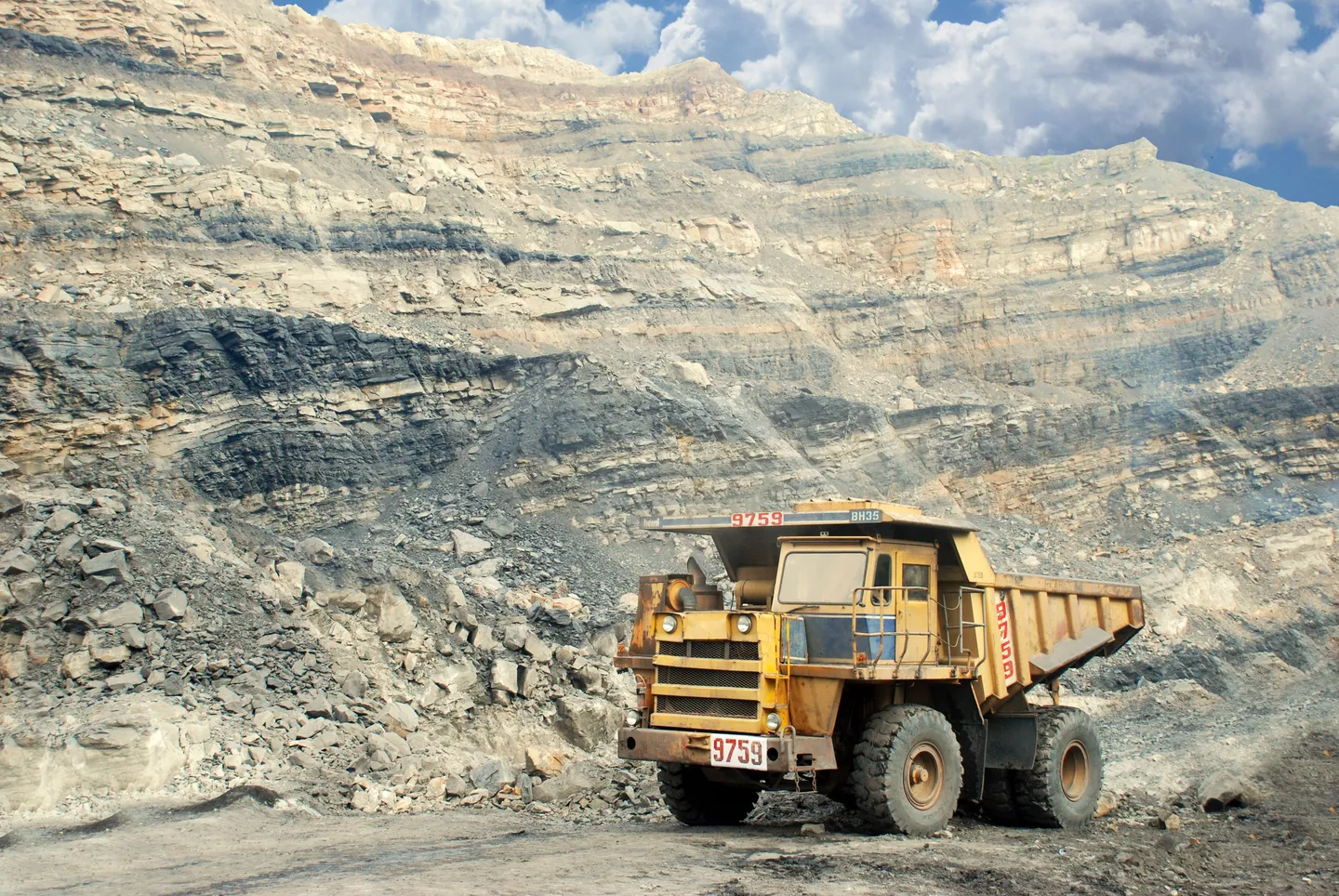 A rigid haul truck at the foot of a terraced open-pit mine face.